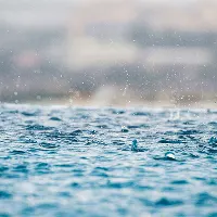 Close-up of raindrops splashing on the surface of blue water, with blurred background.