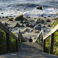 Wooden staircase leading down to a rocky shoreline with ocean waves in the background.