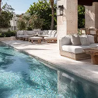 Luxury outdoor poolside lounge with cushioned seating, stone columns, and surrounding greenery.
