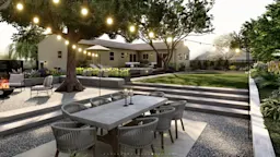 Spacious backyard with long outdoor dining table and chairs under mature trees, next to a modern home.