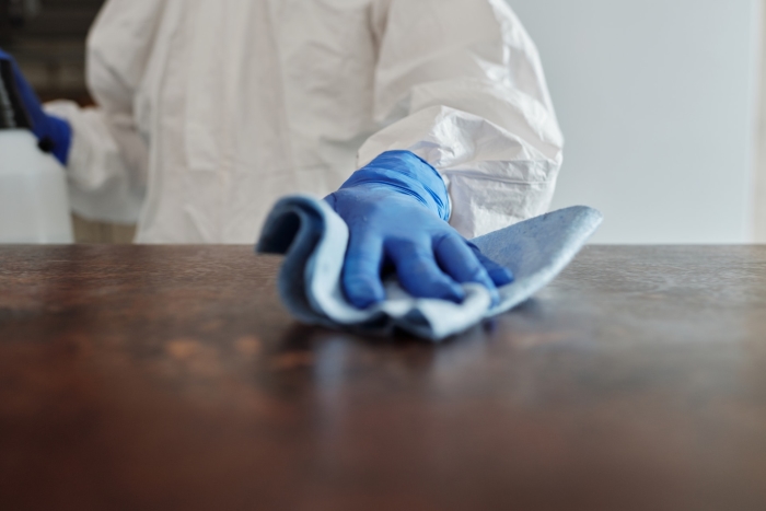 Person in white suit wiping counter with microfiber cloth.