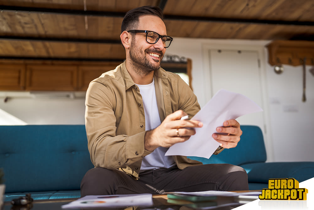 Ein Mann hat einen Zettel in der Hand und lächelt. 