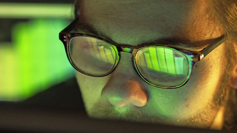 Mann mit Brille sitzt vor grünem Bildschirm