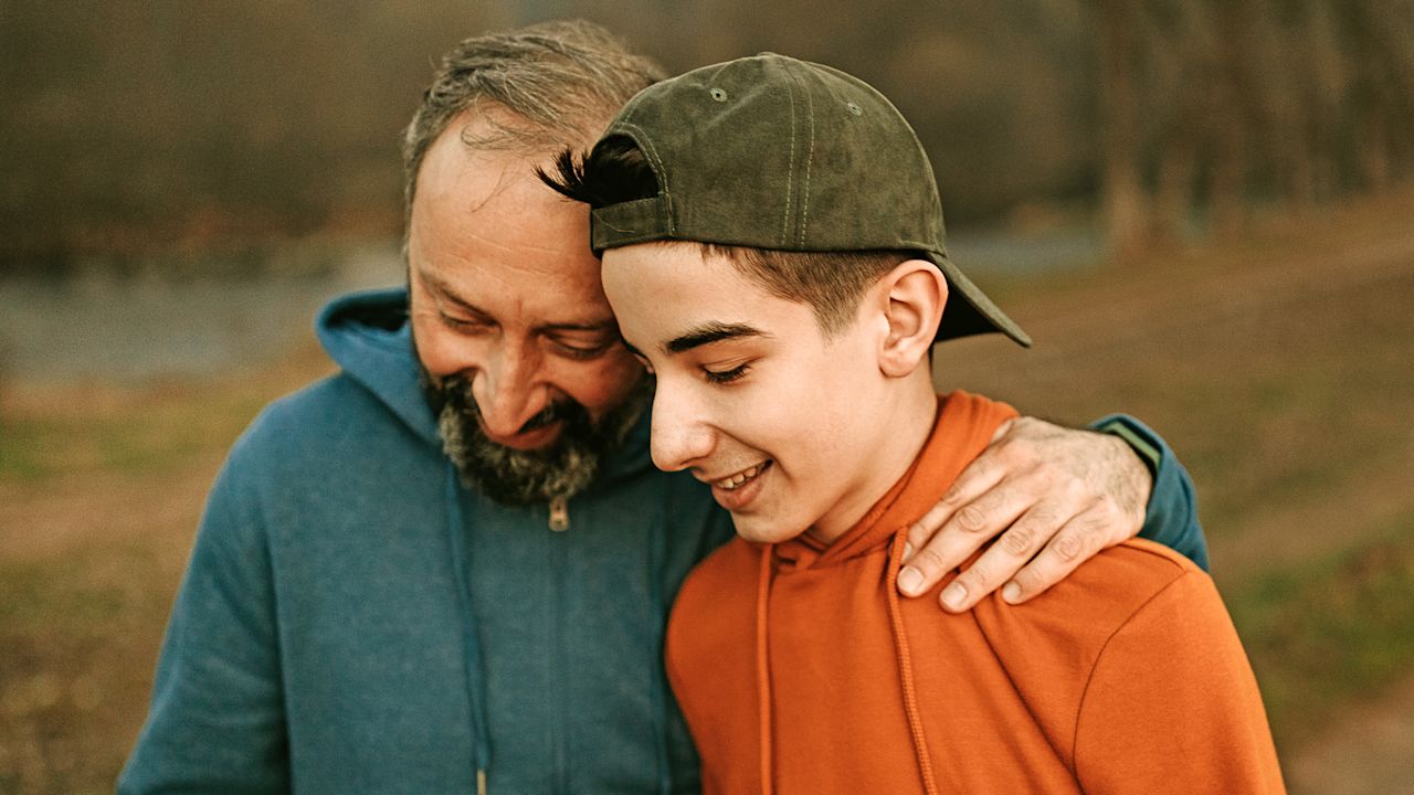 Vater legt seinen Arm um jugendlichen Sohn