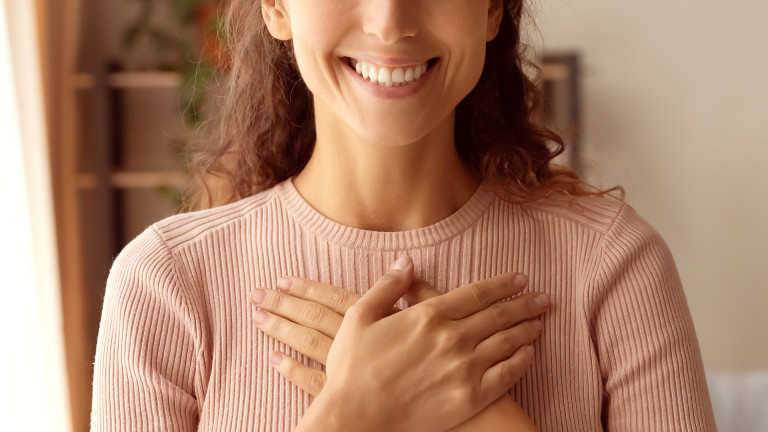 Eine lächelnde Frau legt ihre flachen Hände überkreuzt auf ihren Oberkörper.