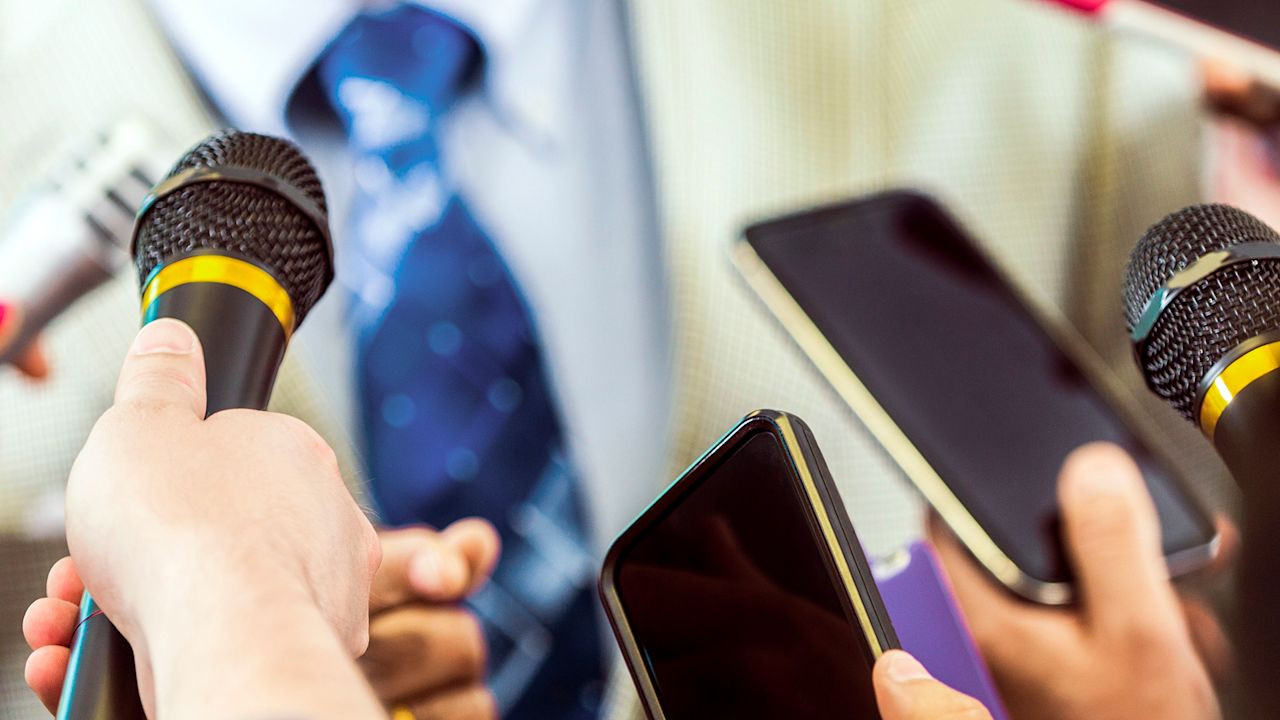 Mikrofone und Smartphones werden einer nicht vollständig sichtbaren Person bei einem Pressetermin für Audioaufnahmen entgegengehalten.