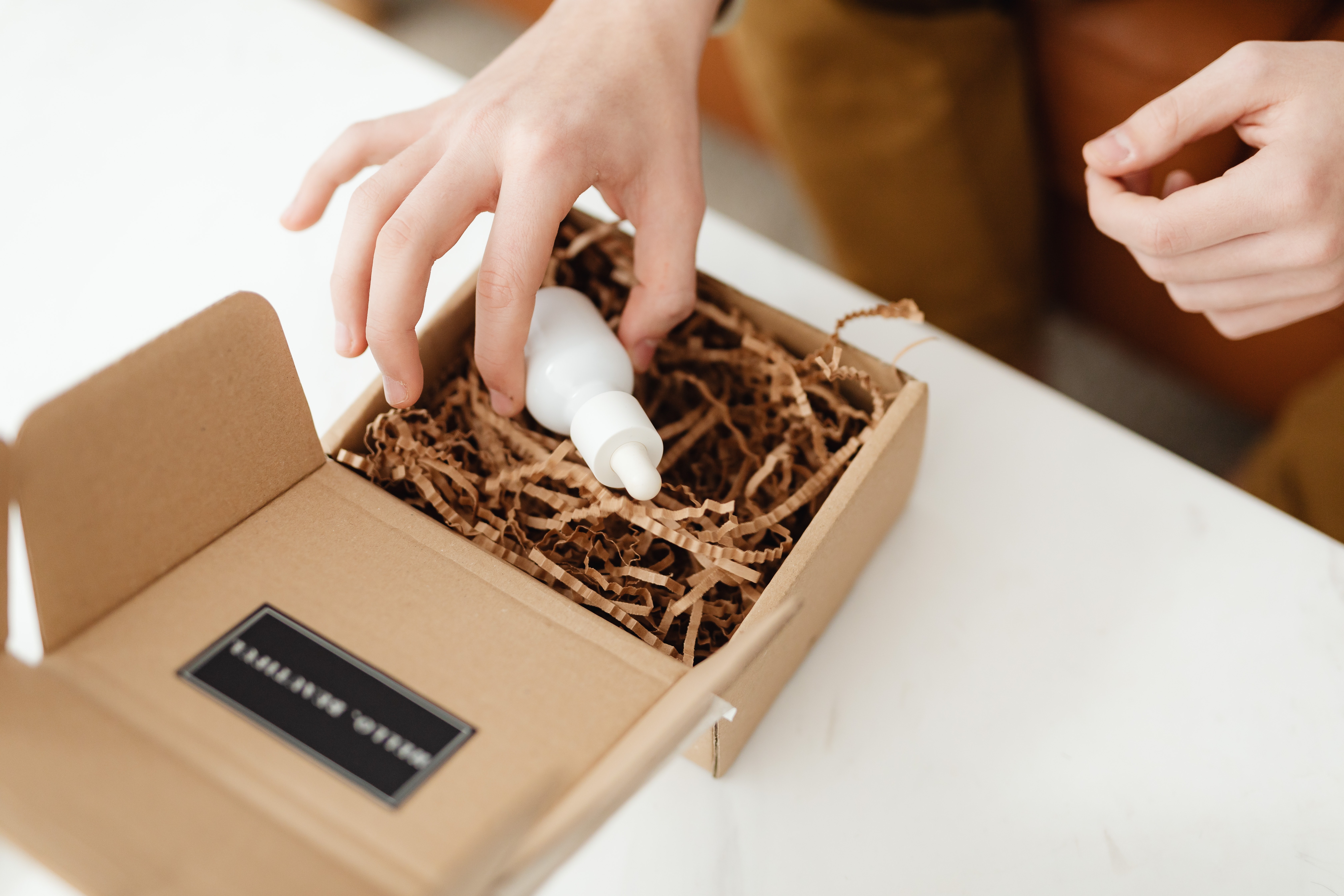 Hands of a Person Holding a Mailer Box That Contains a Plain White Dropper Bottle