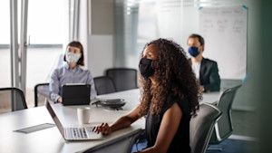 Team of business professionals wearing face mask sitting in office boardroom during a meeting.