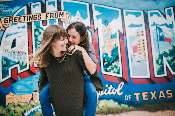 Two people posing playfully in front of a 'Greetings from Texas' mural