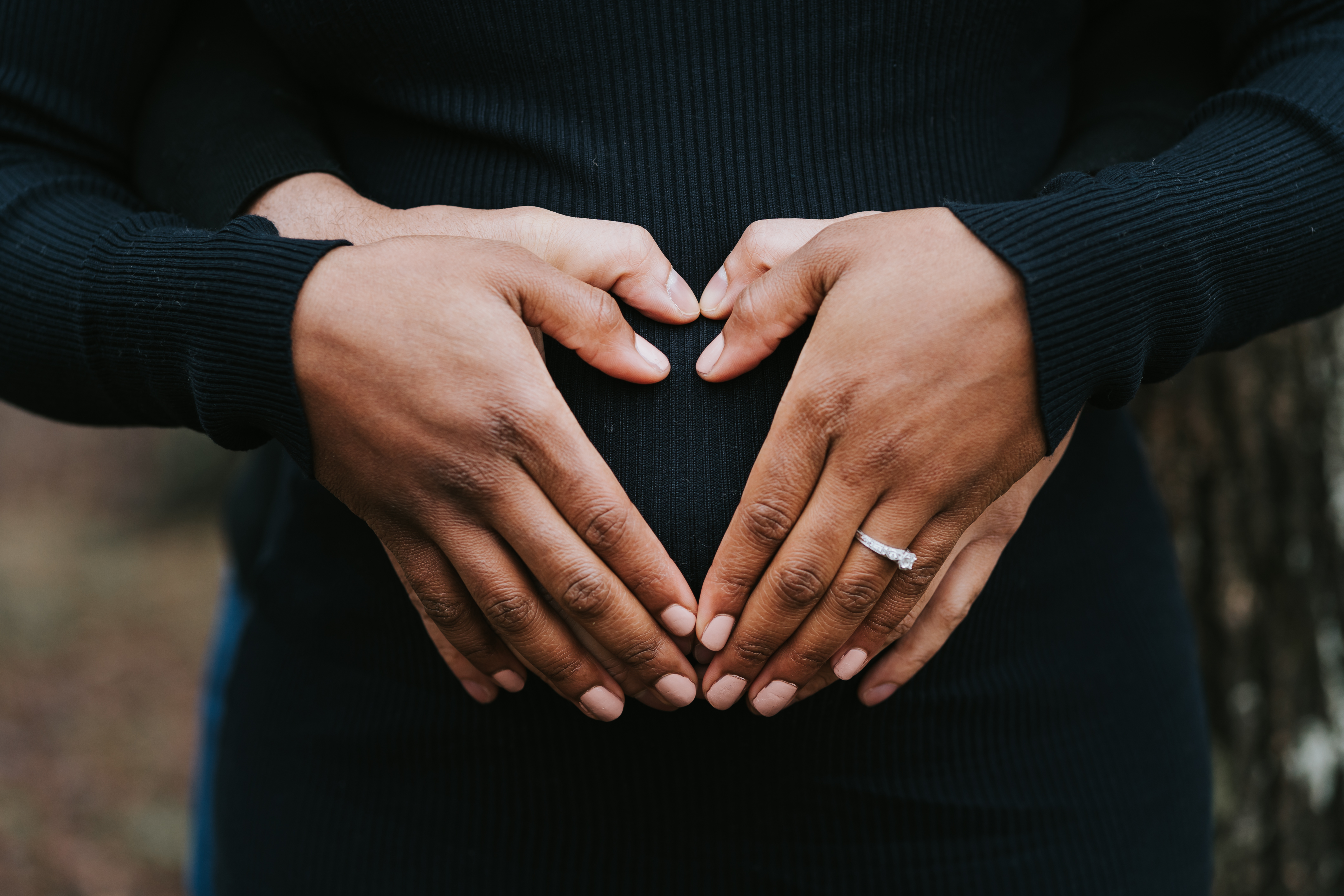 Close-up of a couple's hands forming a heart shape over a pregnant belly, with the mother's engagement ring visible, captured during a Shoott maternity photoshoot.