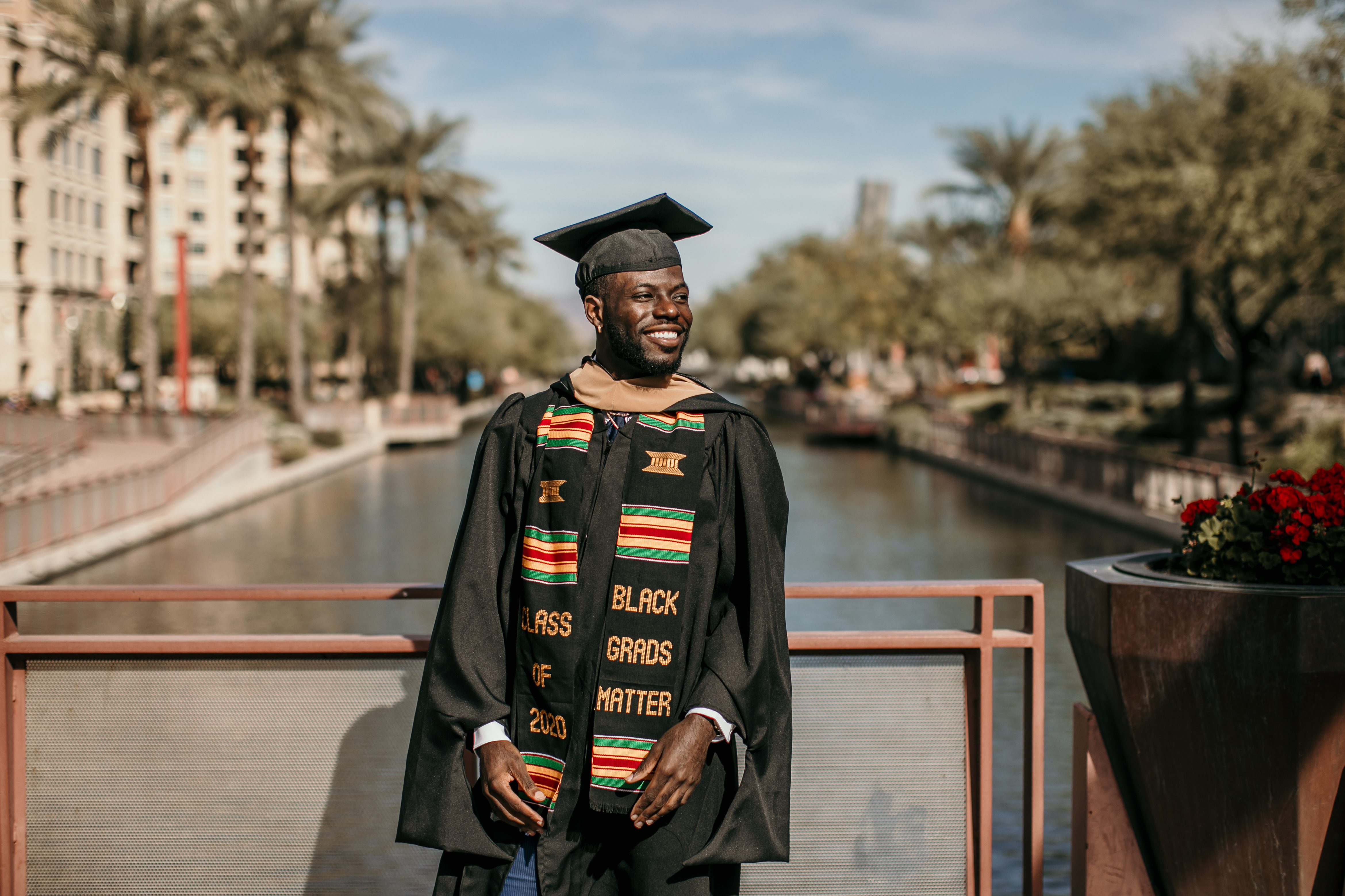 Graduate smiling in cap gown and kente stole by a canal during free professional graduation photo session with Shoott in Atlanta