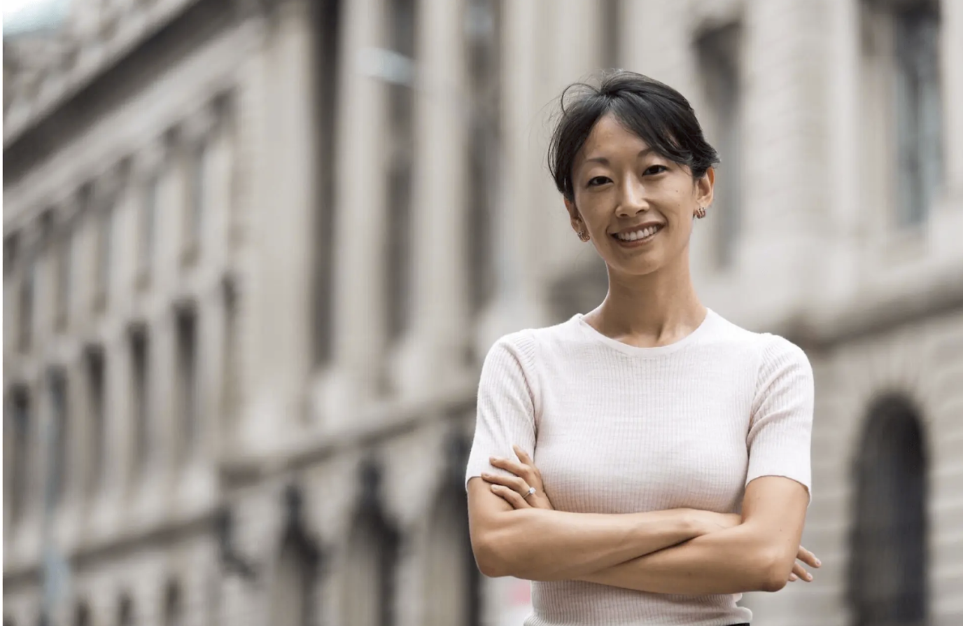 Woman smiling with arms crossed in front of a historic building during free professional headshot photo session with Shoott in Houston  
