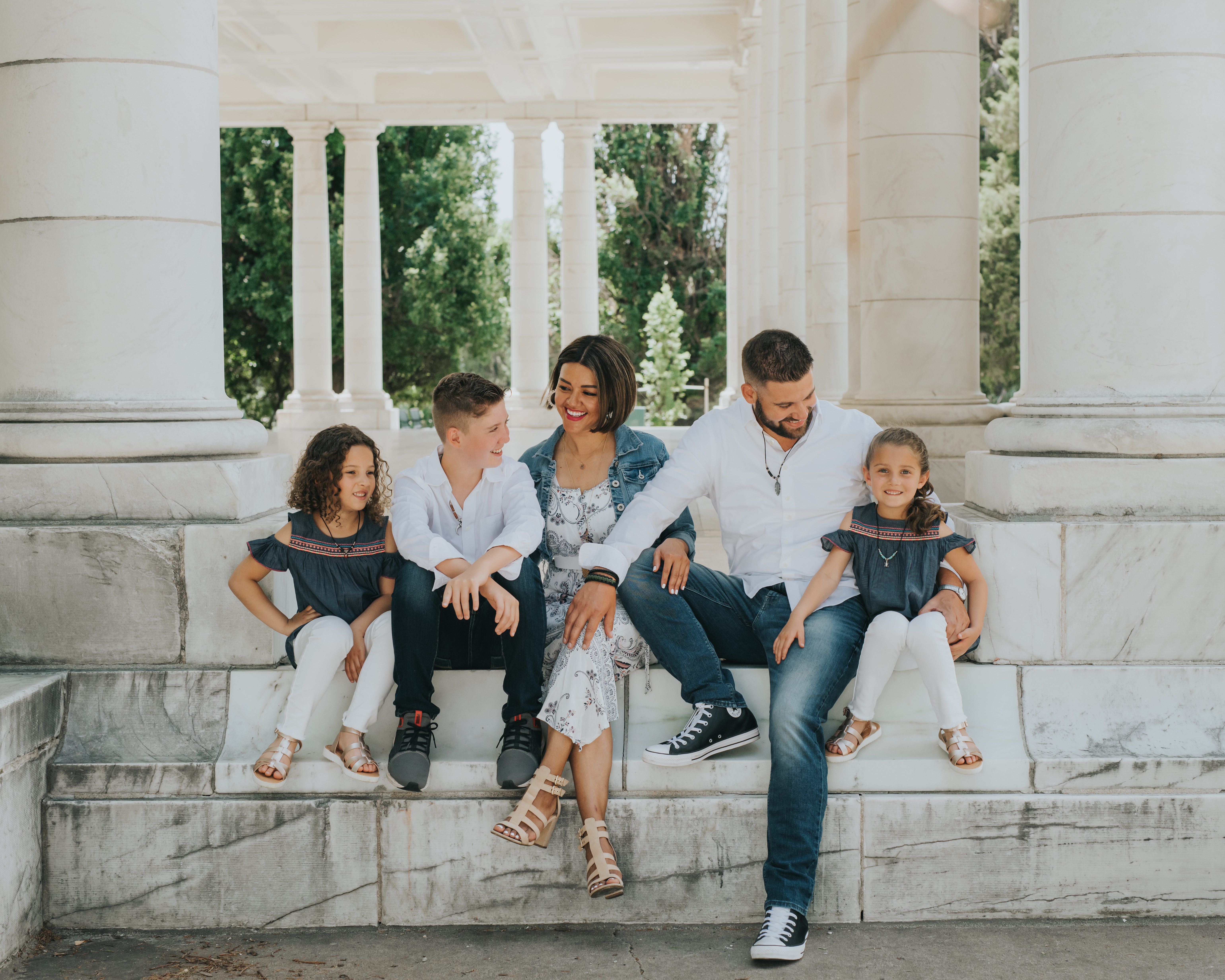Family of five posing on steps during a professional Shoott photo shoot, with white classical columns and greenery in background.