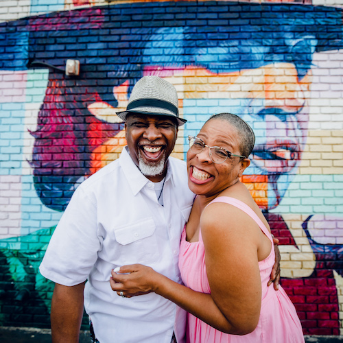A joyful couple embracing and smiling in front of a colorful mural.