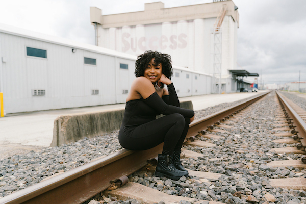 A woman sitting on train tracks with buildings in the background.
