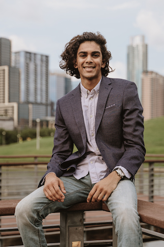 Young man sitting on a railing with city skyline in the background