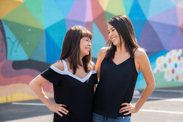 Two women smiling at each other in front of a colorful mural.