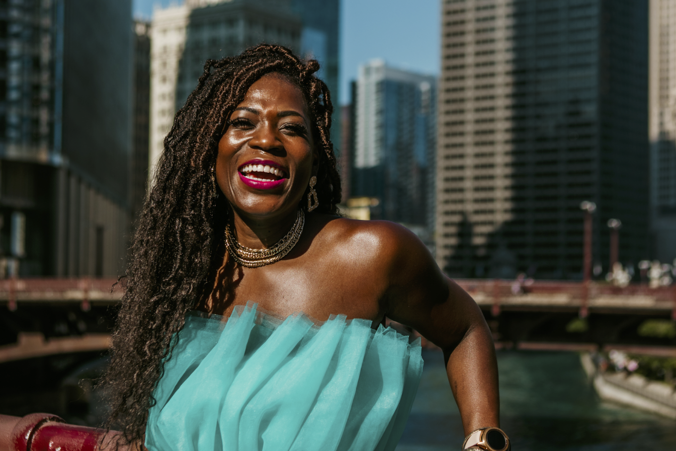 Woman laughing in a turquoise dress with gold jewelry and city skyline behind her during free professional lifestyle photo session with Shoott in Houston