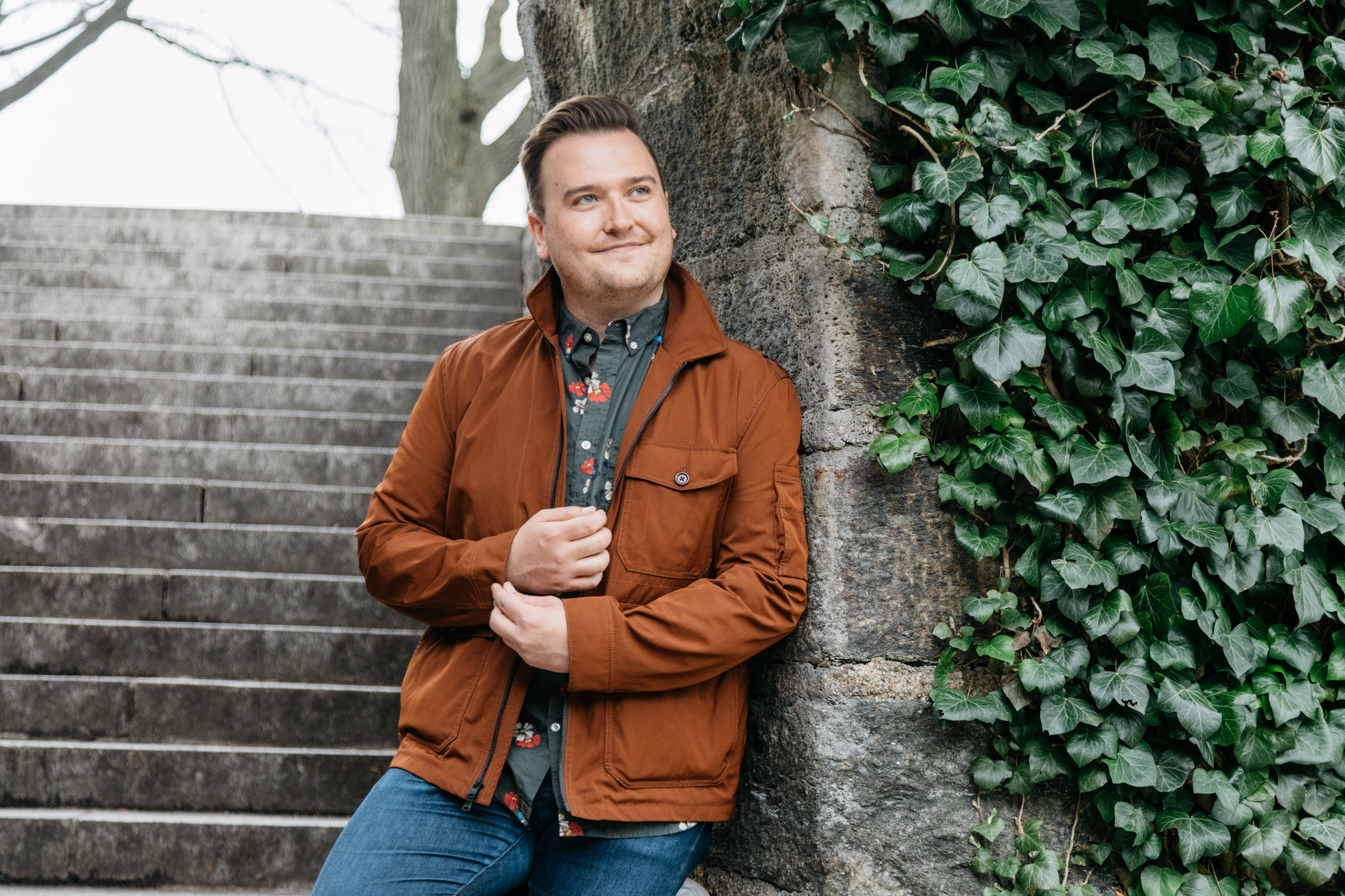 Man posing against stone wall near outdoor steps during a free Shoott dating profile photography session natural light portrait