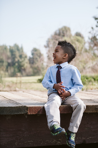 A young boy laughing while sitting on a wooden ledge outdoors.