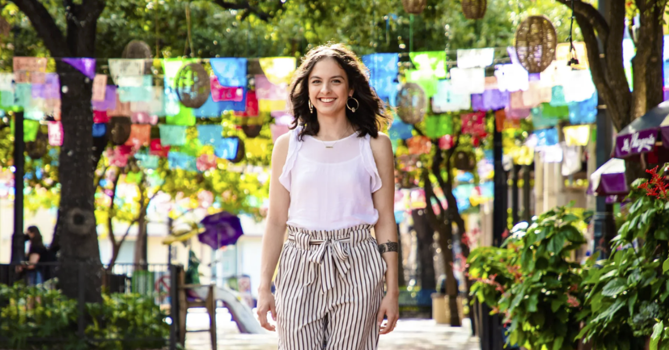 Woman smiling and walking under colorful papel picado banners on a San Antonio street during free professional portrait photo session with Shoott