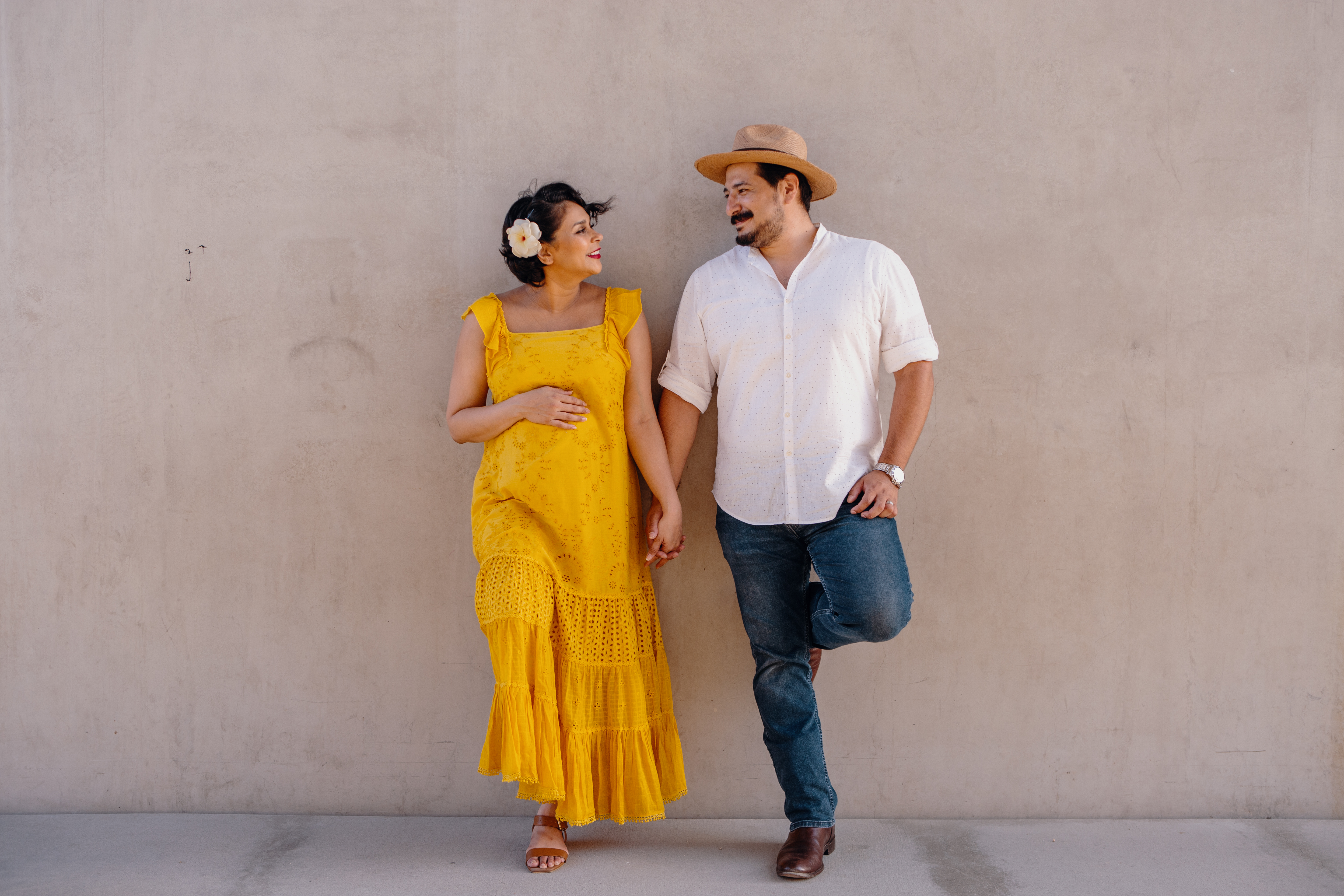 Expecting couple posing together during a professional Shoott maternity photo shoot, against a neutral beige wall.