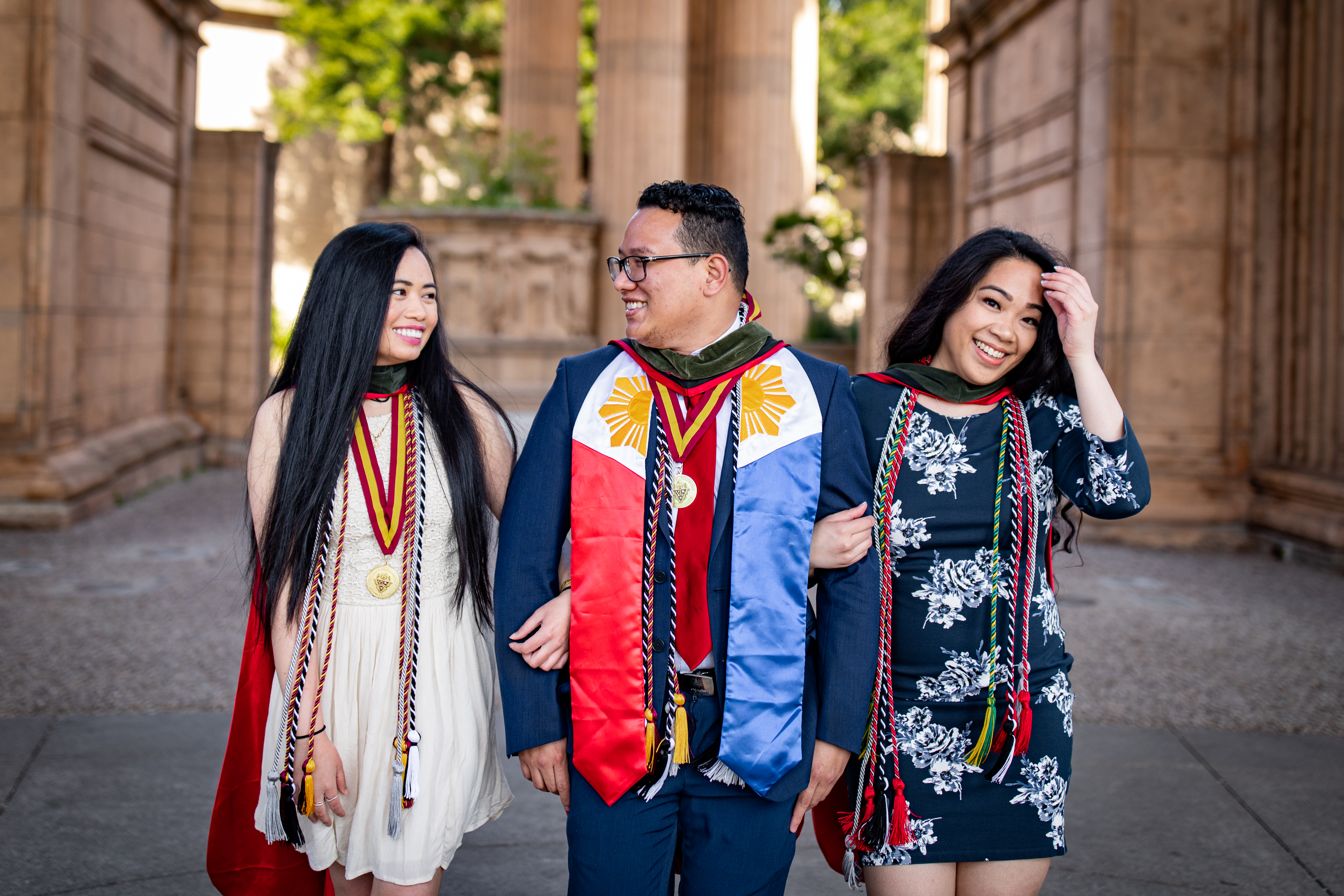Three graduates wearing honor cords and stoles laughing together during a free professional graduation photo session with Shoott