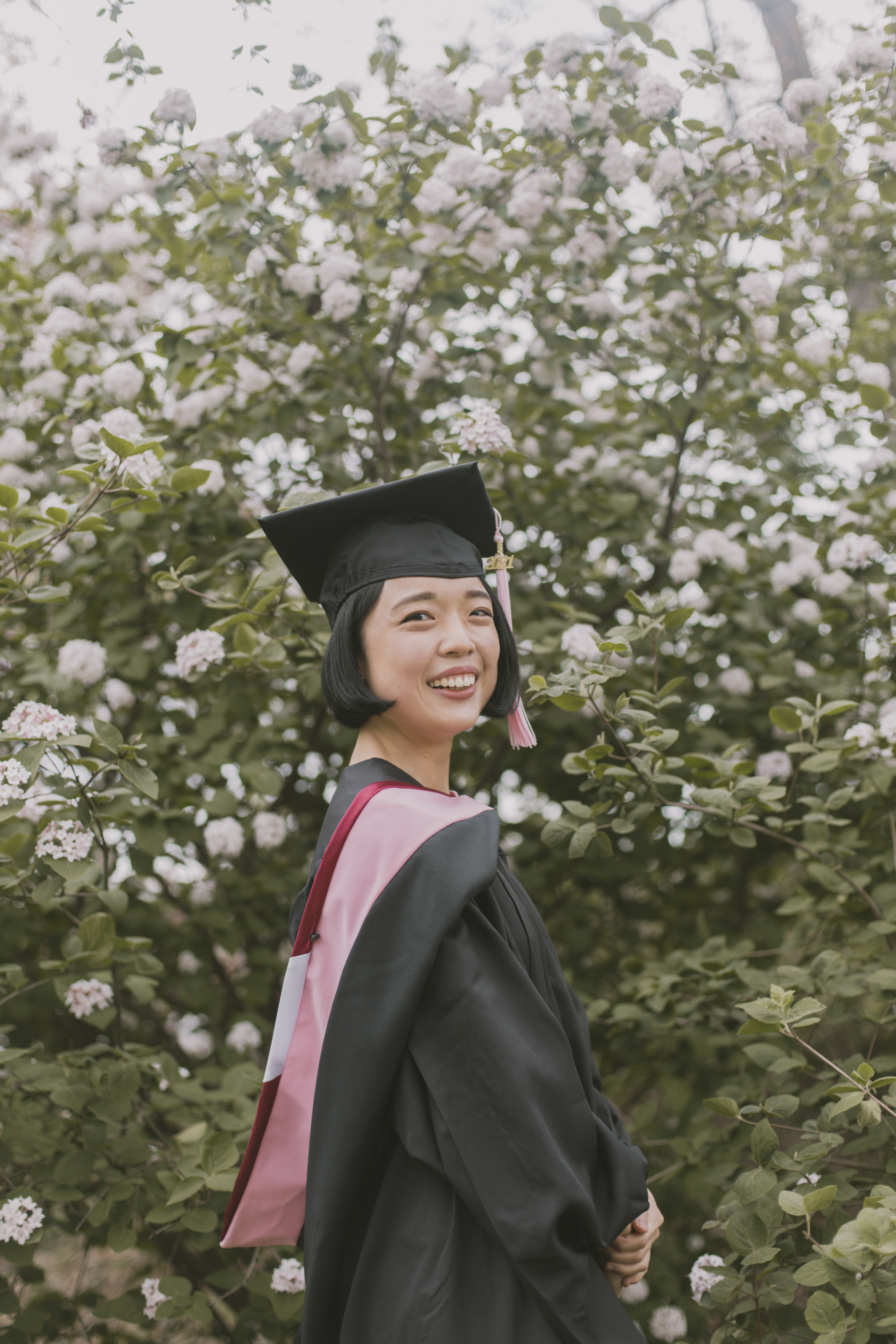 Senior in cap and gown among spring blossoms by a Shoott photographer.