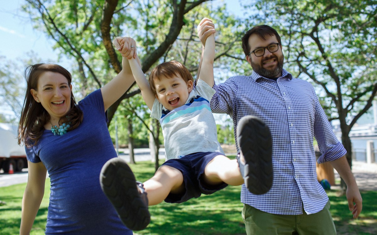 Parents swinging their laughing son between them in a park during a free Shoott lifestyle photography session