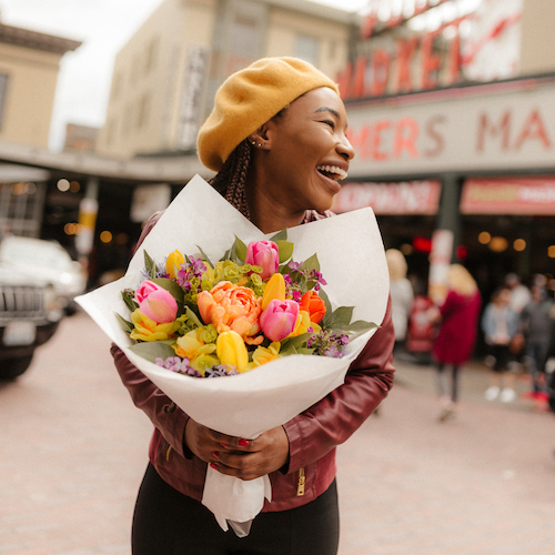A joyful person holding a bouquet of flowers on a city street.
