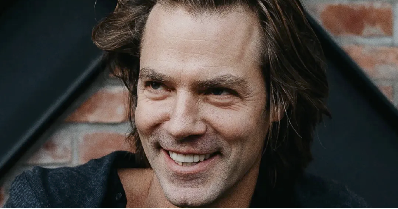 Man with long hair smiling against a brick wall during free professional portrait photo session with Shoott in San Antonio