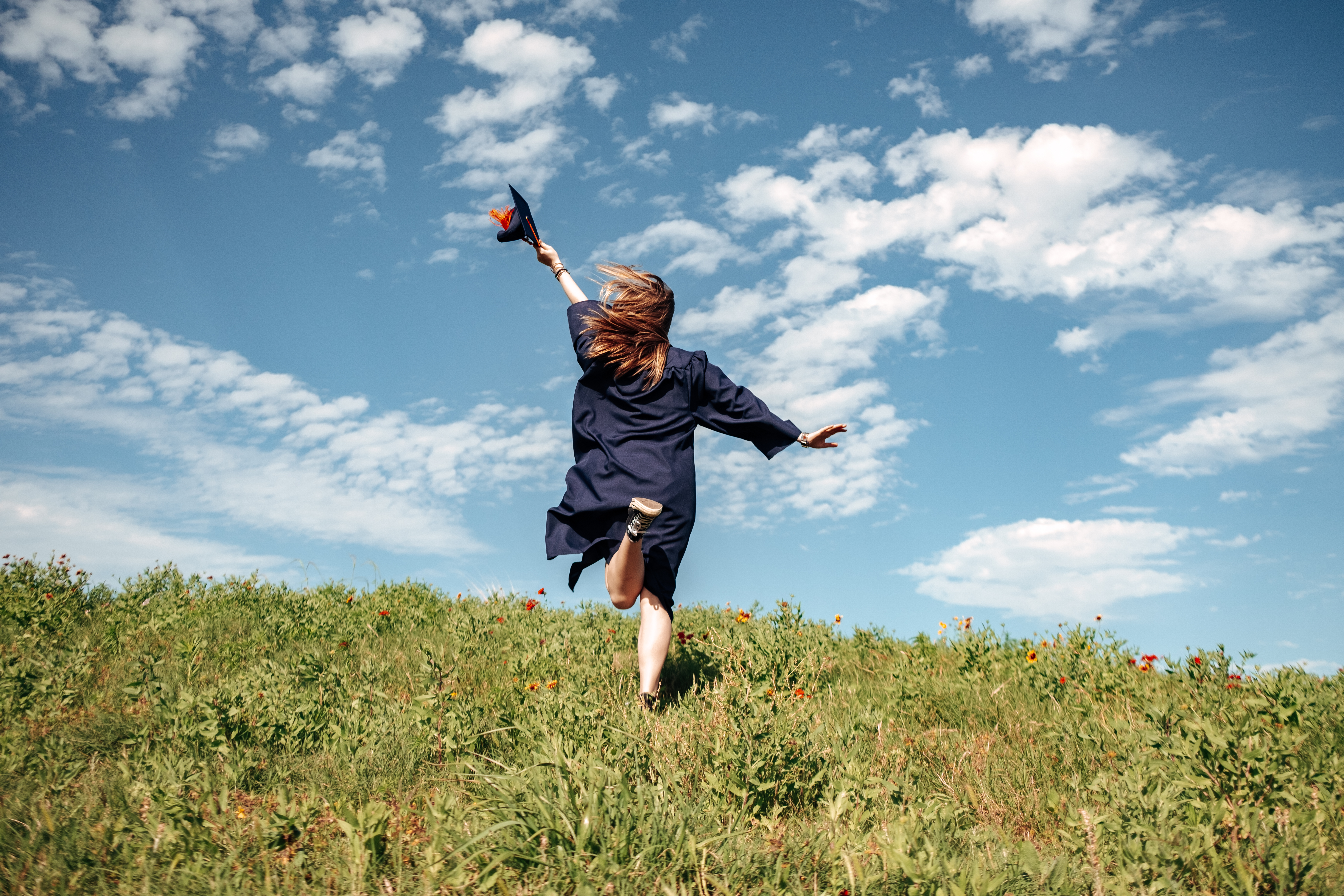 Graduate running with cap in the air during an outdoor Shoott graduation photoshoot