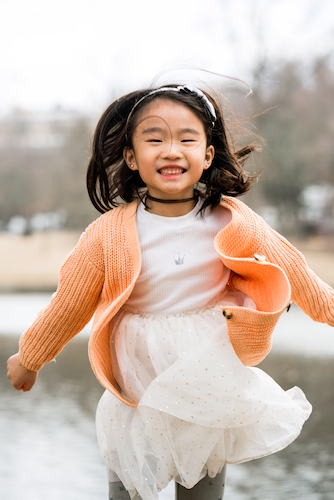 A young girl running and smiling with her hair flying in the air.
