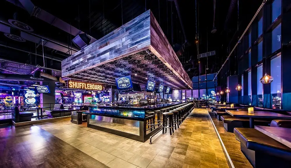 Bar of the Lucky Strike Somerville location with barstools, booths, and a shuffleboard sign in the background.