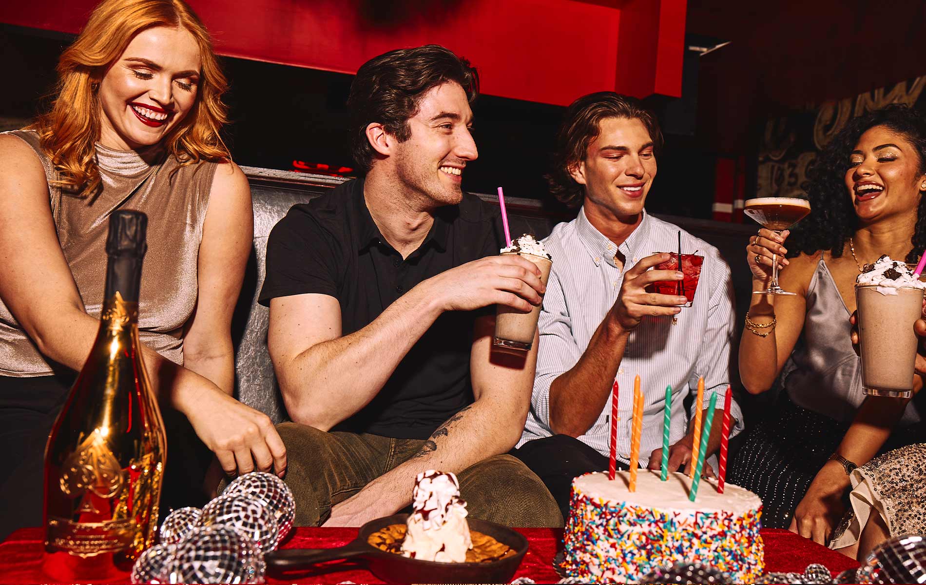 people smiling sitting in a booth with cocktails and a birthday cake