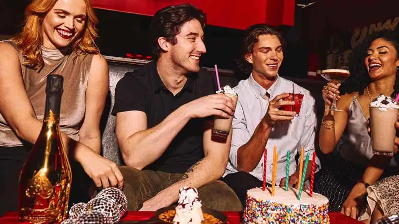 A group of people celebrating with drinks and a birthday cake.