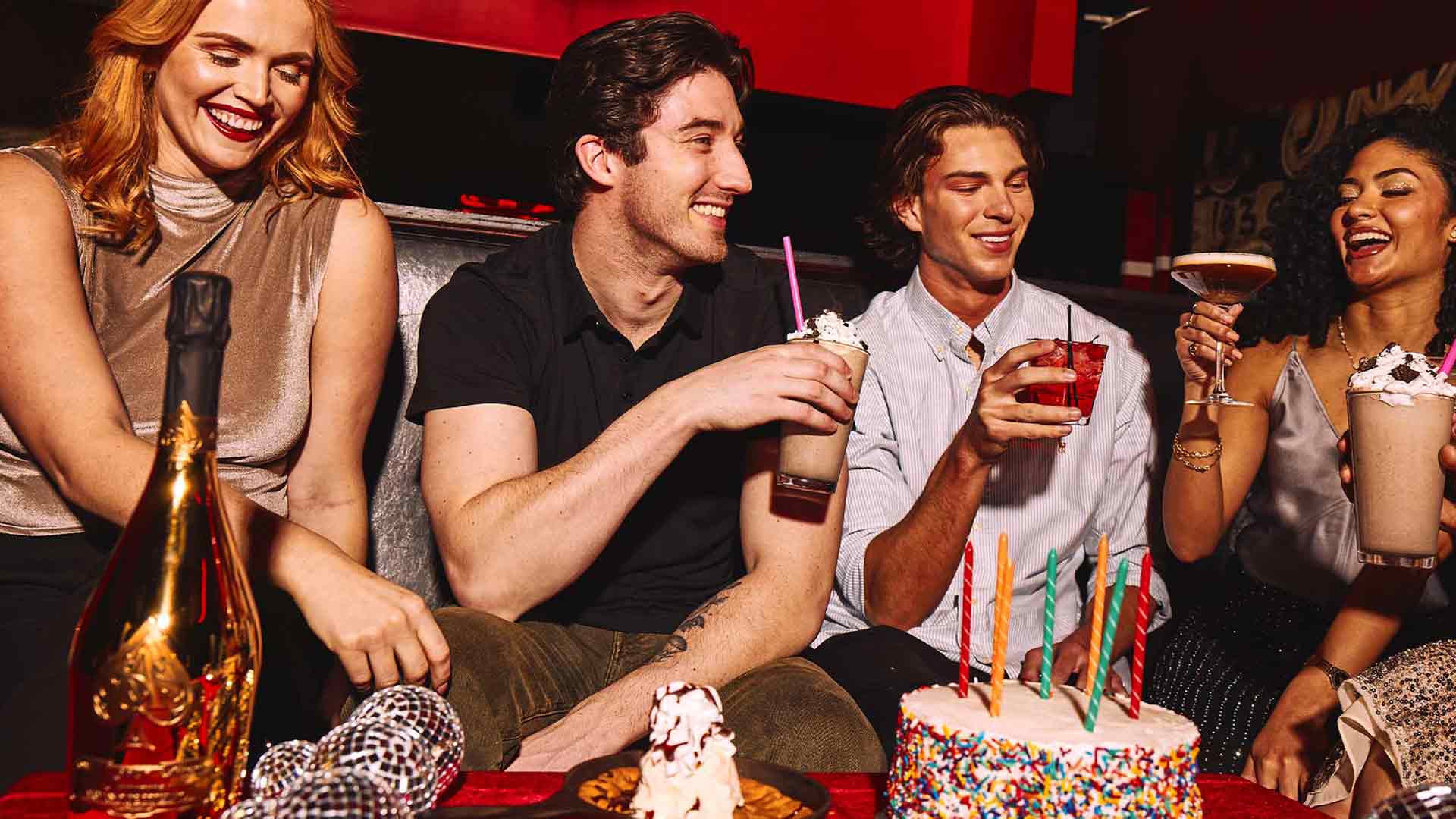 A group of people celebrating with drinks and a birthday cake.