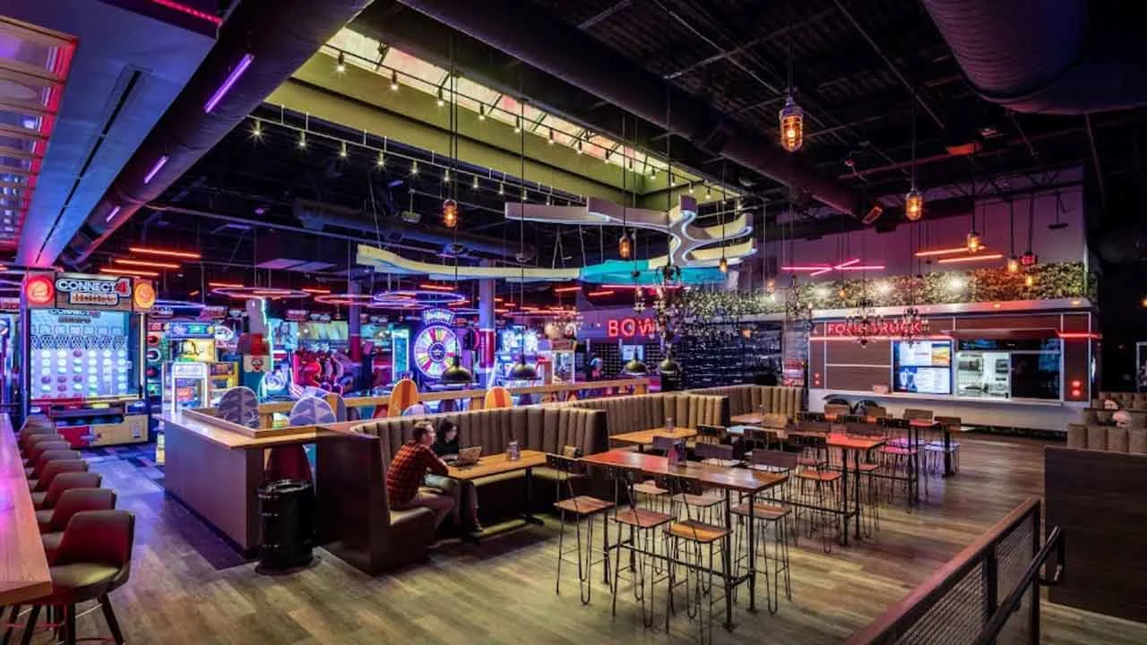 Bar and lounge seating area at Lucky Strike Dania Beach with arcade games, food truck counter, and neon signage