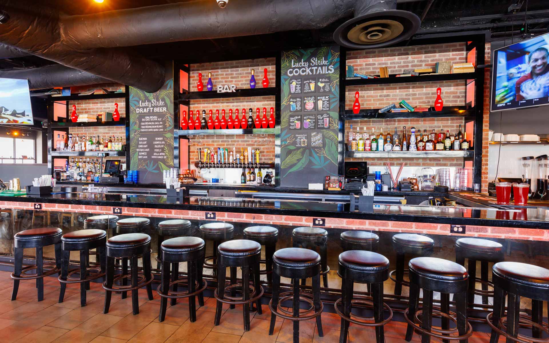 Clean, modern bar with exposed brick, backlit shelving, and Lucky Strike-branded menu boards. A more casual, approachable bar setup that still feels elevated and on-brand.