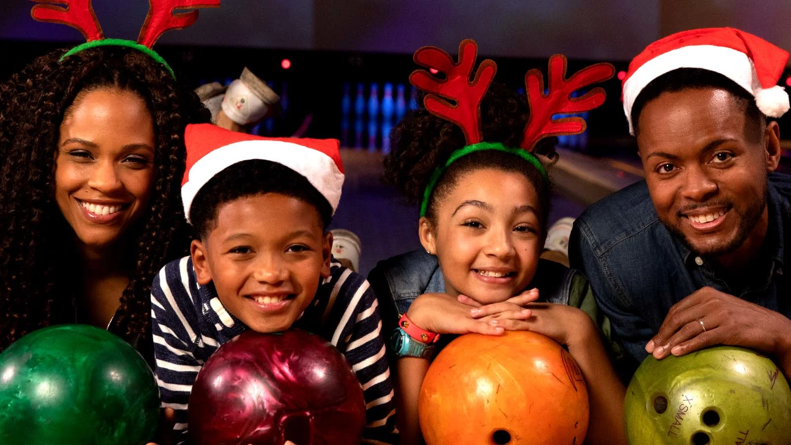 Family with bowling balls wearing Santa hats and reindeer antlers.