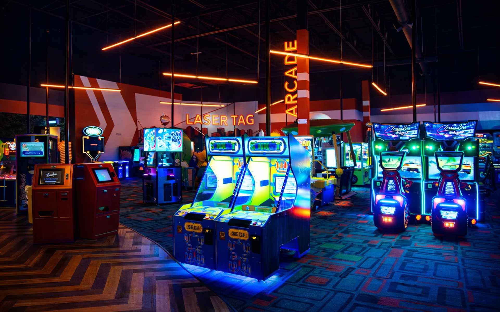 Arcade area with neon-lit racing games, claw machines filled with prizes, and interactive trivia stations in a vibrant Lucky Strike entertainment venue