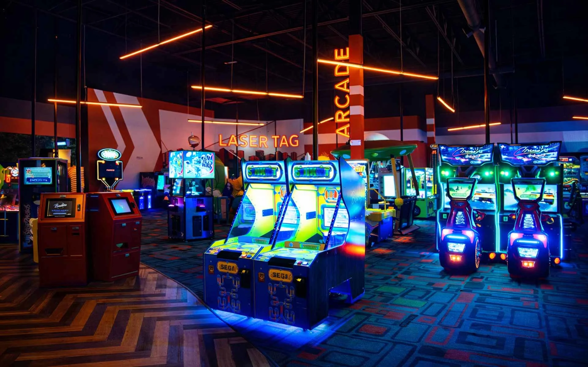 Arcade area with neon-lit racing games, claw machines filled with prizes, and interactive trivia stations in a vibrant Lucky Strike entertainment venue