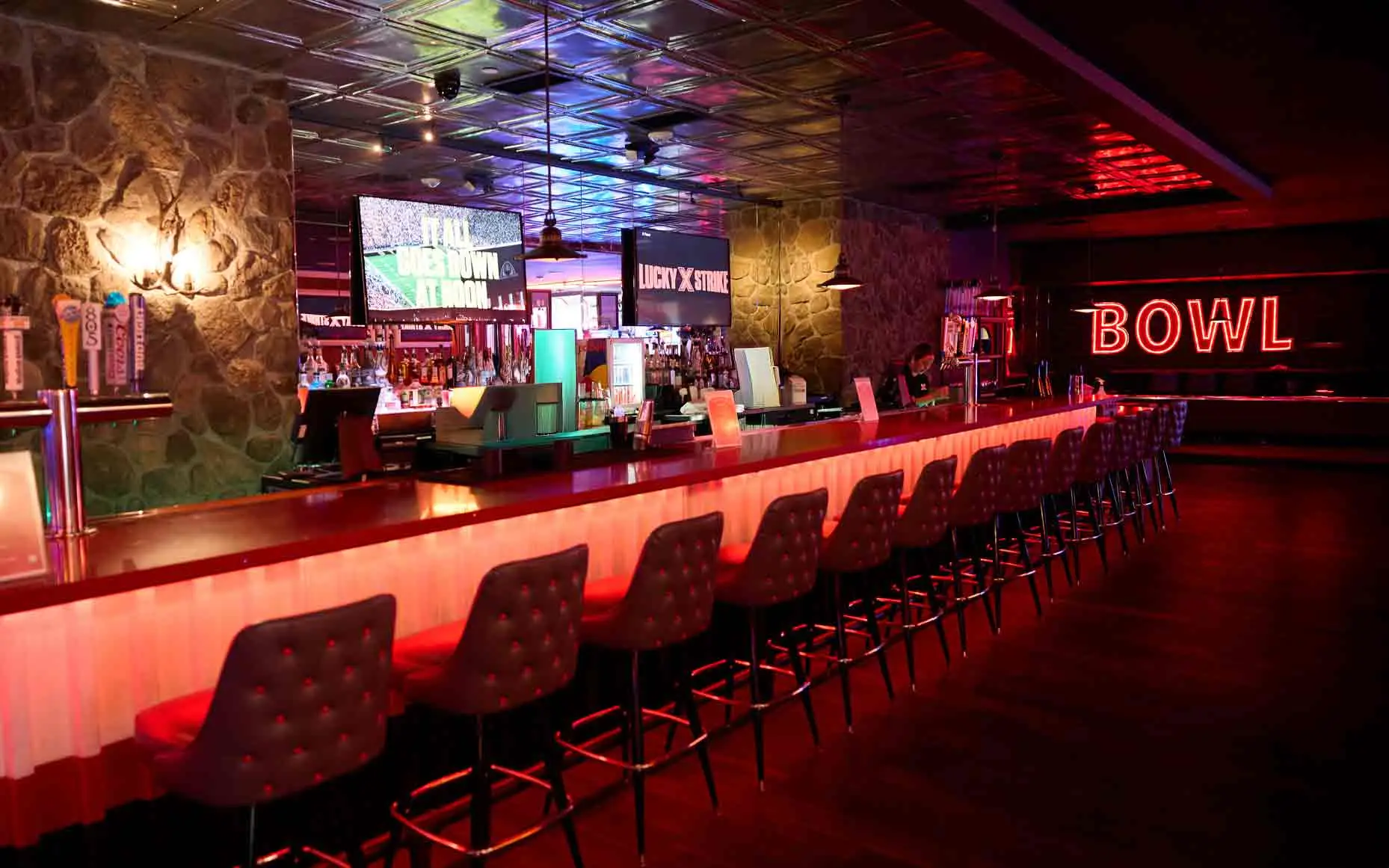 Full bar with red neon Bowl sign, overhead screens, and tufted bar seating at Lucky Strike Los Angeles