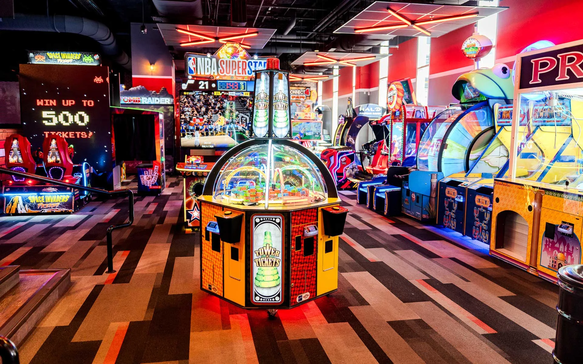 Neon-lit arcade at Lucky Strike Atlantic Station featuring a central prize game surrounded by colorful ticket and racing machines, alongside vibrant lighting and a high-energy, modern entertainment vibe.