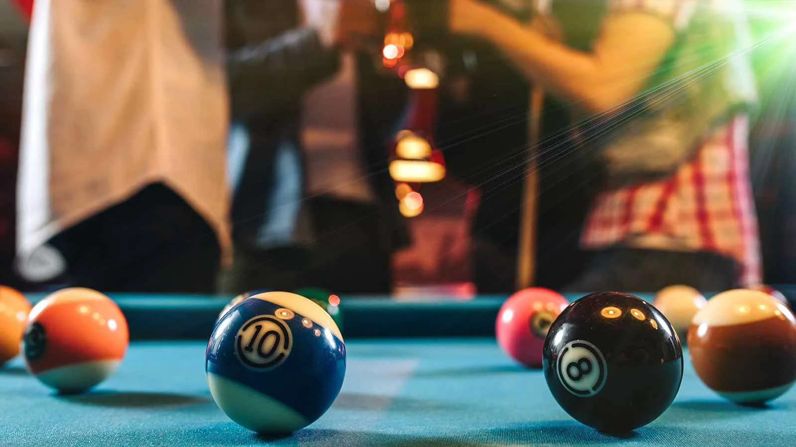 Billiards table with balls in the foregound and people socializing in the background