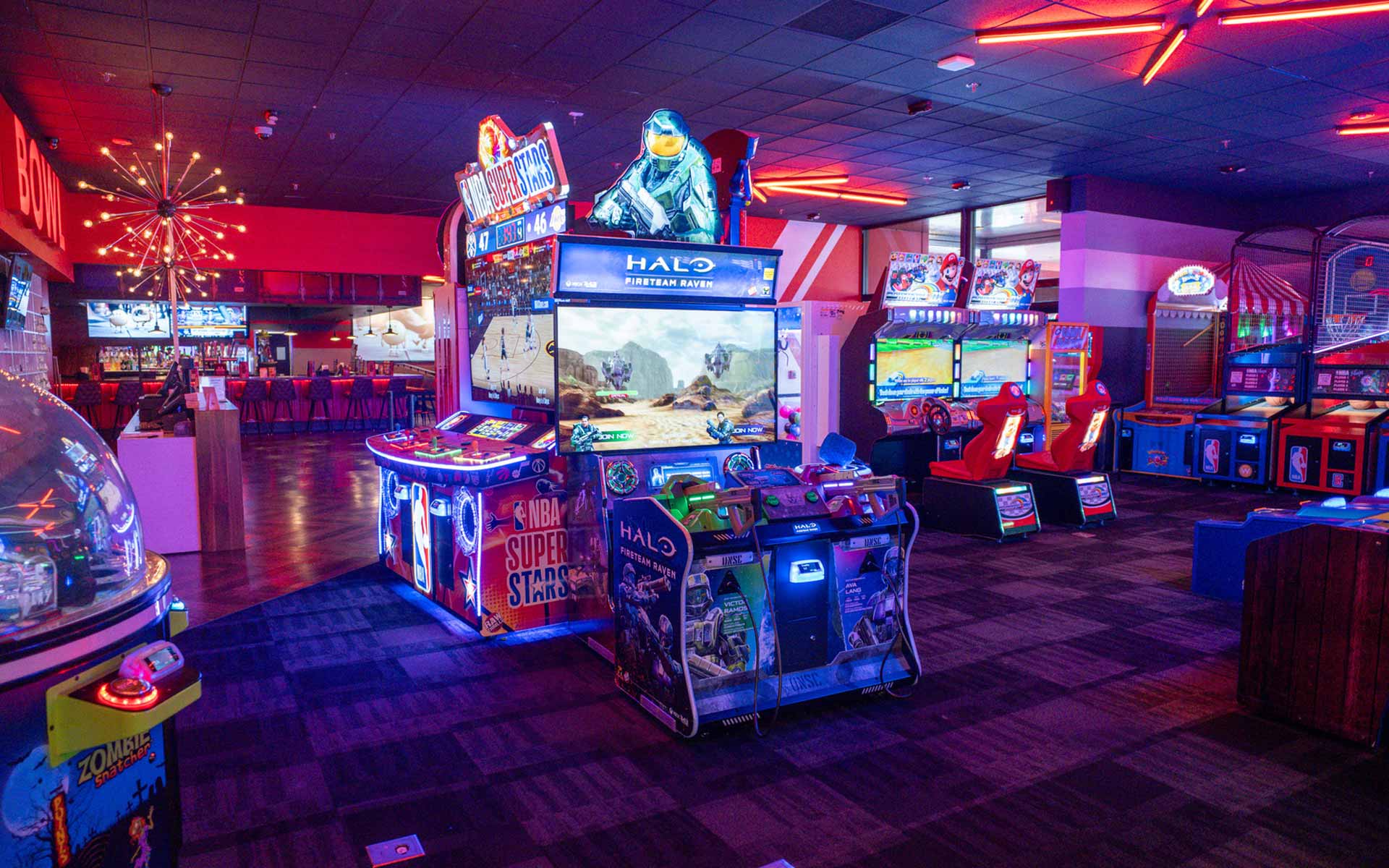 High-energy arcade space with immersive games like Halo Fireteam Raven and racing simulators, surrounded by neon lighting and open sightlines to the bar.