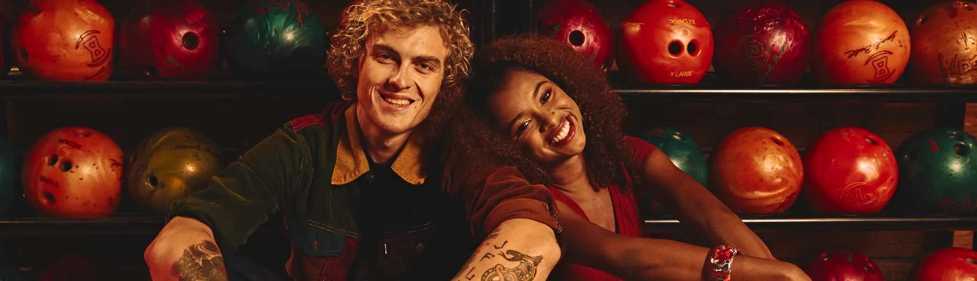 Couple sitting and smiling in front of a bowling ball rack at Lucky Strike.