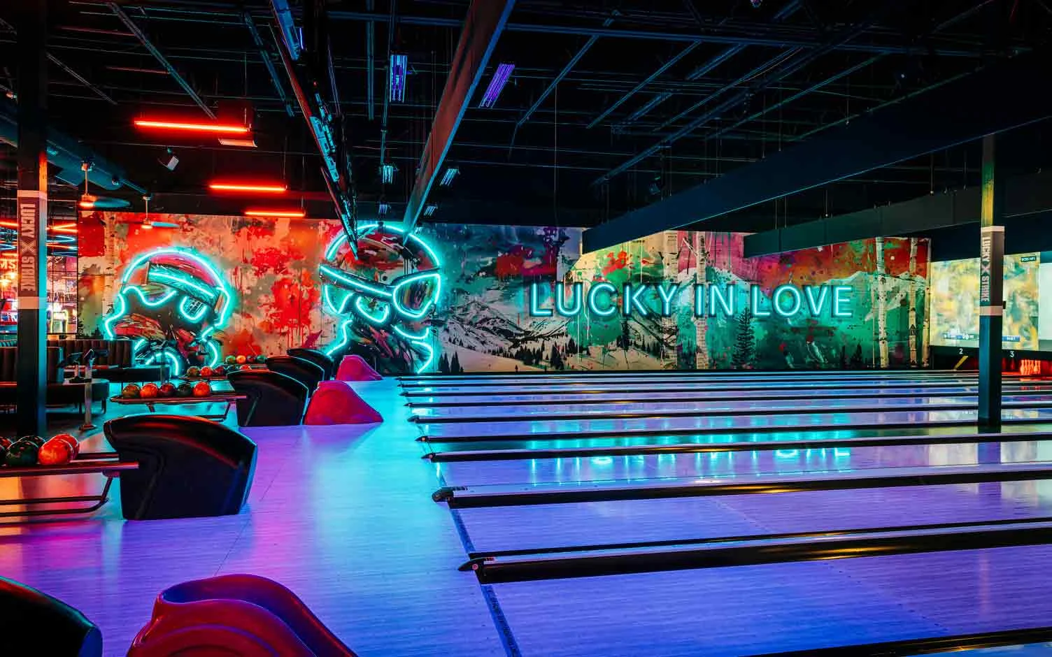 Colorful bowling balls on return rack with bowling center and neon lights in the background.