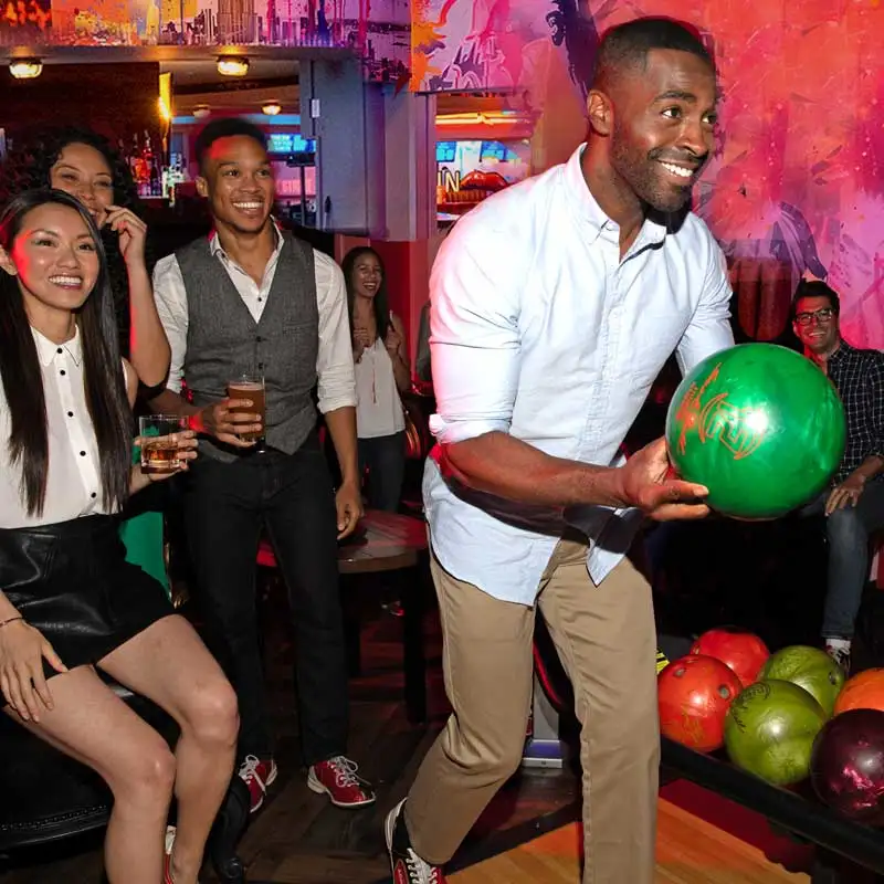 Group of coworkers enjoying a corporate bowling event with drinks and lane-side lounge seating
