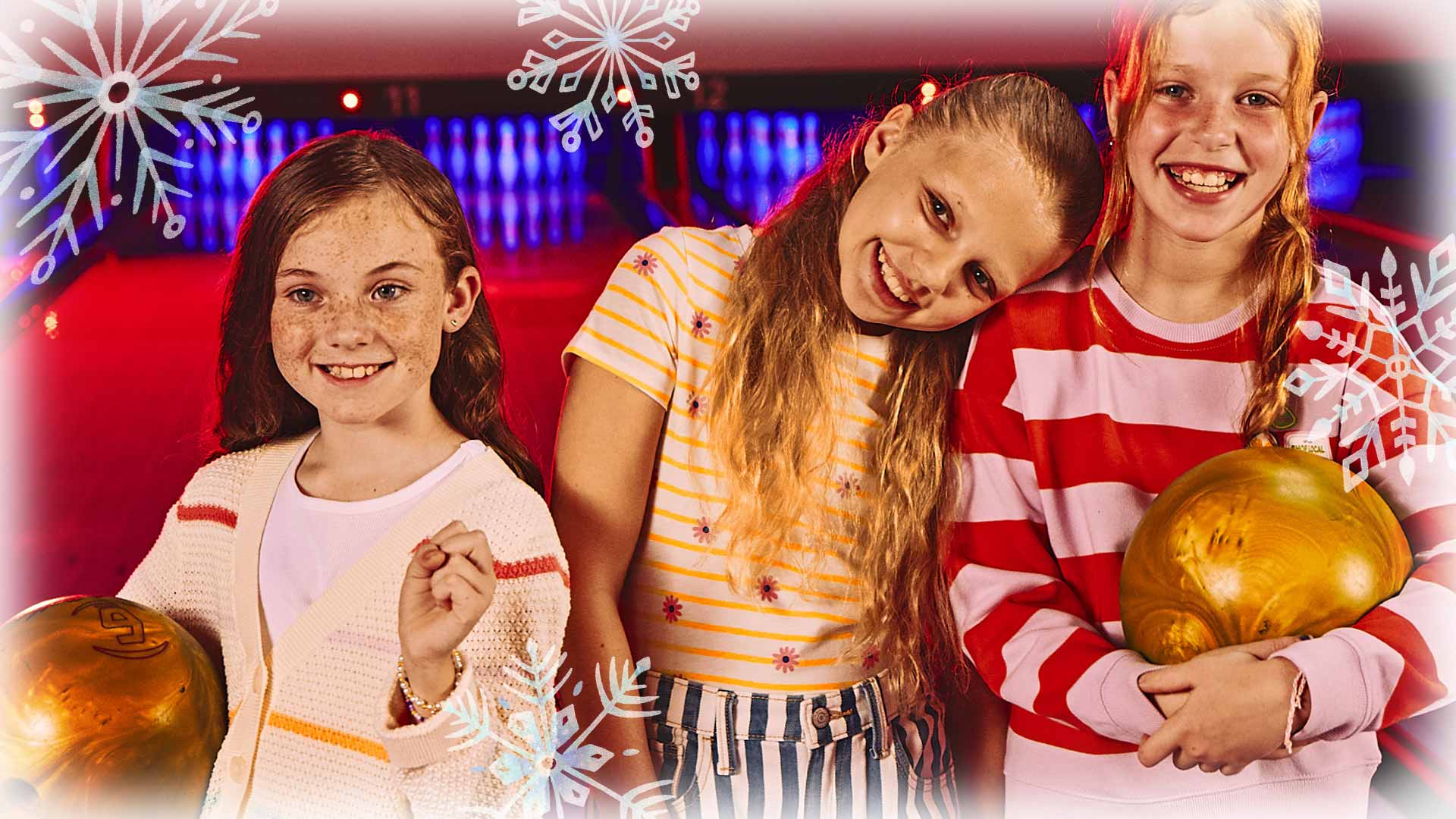 Three kids holding bowling balls with bowling lanes in the background.